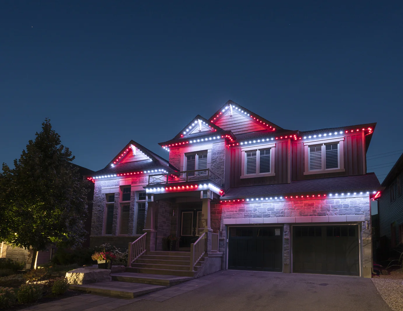 Stone home lit in red and white permanent holiday lighting